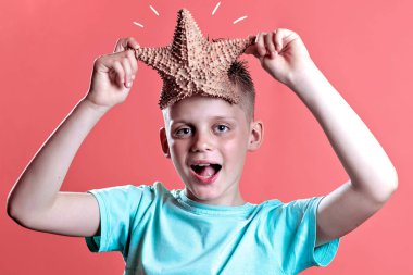 Sarı bir arka plan üzerinde bir denizyıldızı tutan hafif bir t-shirt bir çocuk