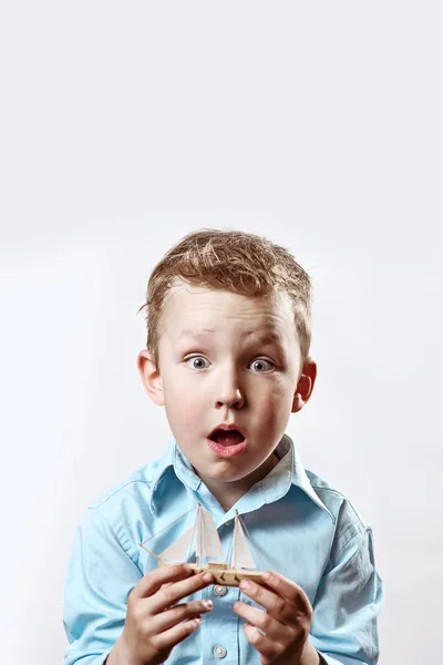 Un ragazzo sorpreso con una camicia blu che tiene una barca tra le mani su uno sfondo chiaro — Foto Stock