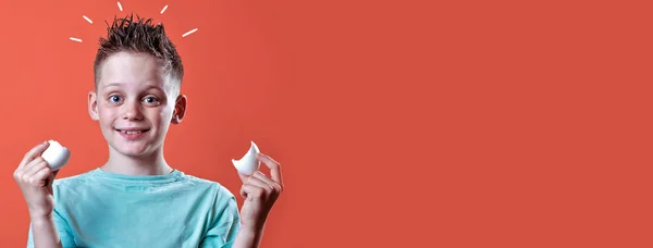 Menino alegre em uma camiseta leve segurando um ovo quebrado em um fundo colorido — Fotografia de Stock