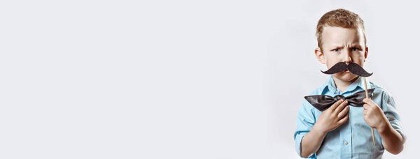 frowning serious boy in a light shirt put a mustache on a stick and a bow tie on his face to make him look older.