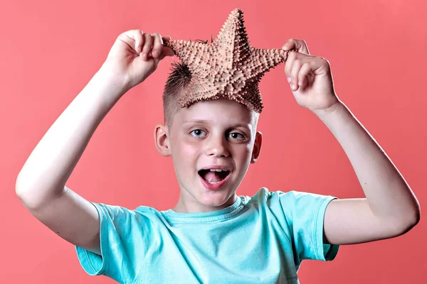 A boy in a light t-shirt holding a starfish on a yellow background — Stock Photo, Image