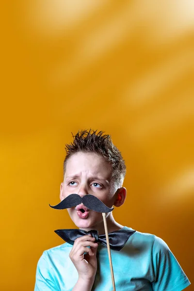 Dreng i en let t-shirt med overskæg og bue synger og siger sjovt - Stock-foto