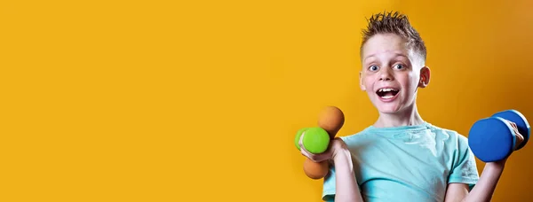 A boy in a bright t-shirt with dumbbells on a yellow background — Stock Photo, Image