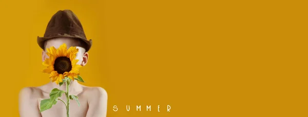 En sommerdreng med en gul solsikke dækker sit ansigt - Stock-foto