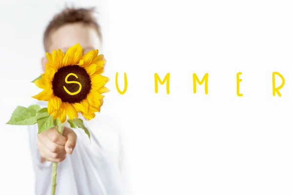 A summer boy in a light t-shirt with a yellow sunflower covers his face — Stock Photo, Image