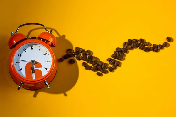 Grãos de café em despertador laranja no fundo amarelo — Fotografia de Stock