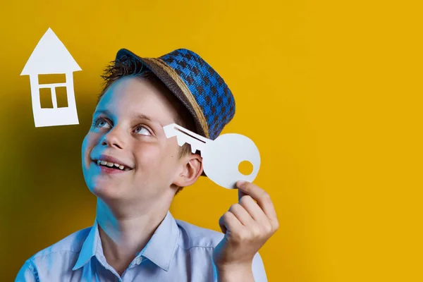 Un niño alegre con una casa de cartón y una llave sobre un fondo de color brillante — Foto de Stock