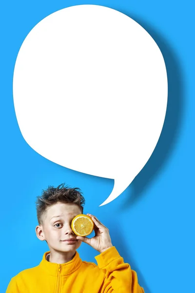 Niño en una chaqueta de color amarillo brillante con un limón en la mano sobre un fondo azul — Foto de Stock