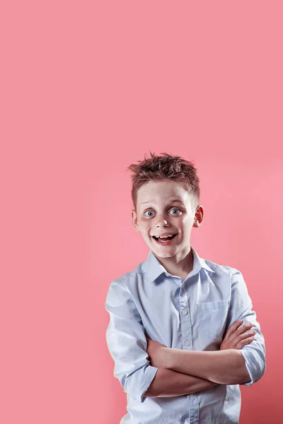 Un niño alegre se para y sonríe con una camisa ligera sobre un fondo de color brillante — Foto de Stock