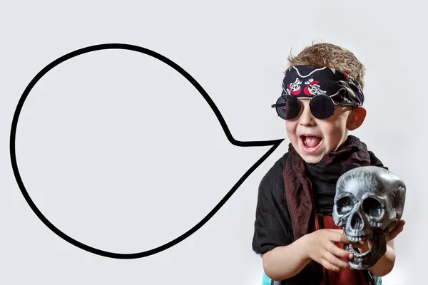 Un niño rockero en gafas negras, bufanda, bandana y con un cráneo en las manos sobre un fondo claro — Foto de Stock
