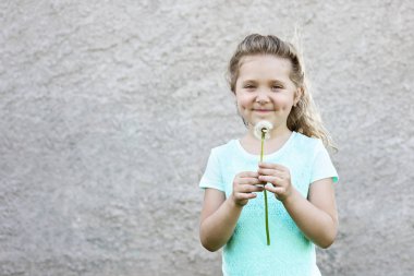hafif bir t-shirt mutlu gülümseyen kız elinde bir karahindiba tutar ve bulanık bir duvara karşı bir dilek yapar