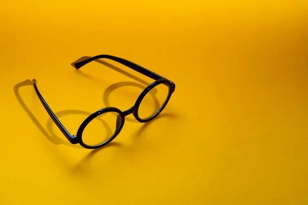 Óculos redondos pretos em um fundo amarelo com sombra dura — Fotografia de Stock