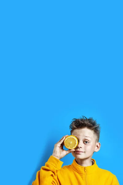 Boy in a bright yellow jacket with a lemon in his hand on a blue — Stock Photo, Image