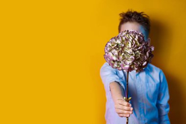 parlak renkli bir arka plan üzerinde yüzünün önünde bir buket tutan bir çocuk