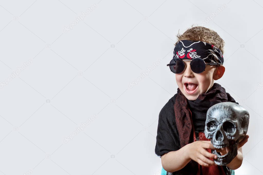 a boy rocker in black glasses, scarf, bandana and with a skull in his hands on a light background