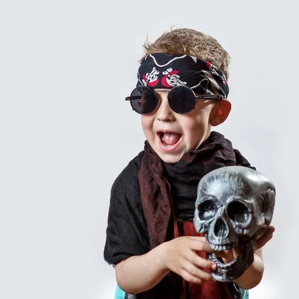 A boy rocker in black glasses, scarf, bandana and with a skull in his hands on a light background — Stock Photo, Image
