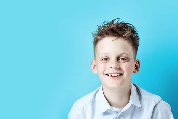 Un niño alegre se para y sonríe con una camisa ligera sobre un fondo de color brillante — Foto de Stock