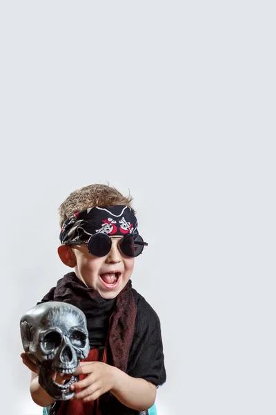 A boy rocker in black glasses, scarf, bandana and with a skull in his hands on a light background — Stock Photo, Image