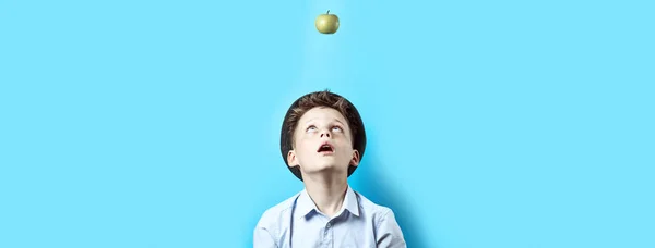 Překvapenej kluk v lehké košili vzhlíží. Tam na něm padá zelený jablko, jako symbol skvělých nápadů — Stock fotografie