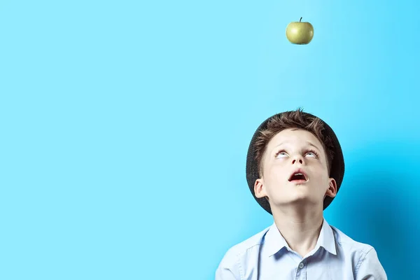 Overrasket dreng i en let skjorte kigger op. Der på ham falder grøn Apple, som et symbol på gode ideer - Stock-foto