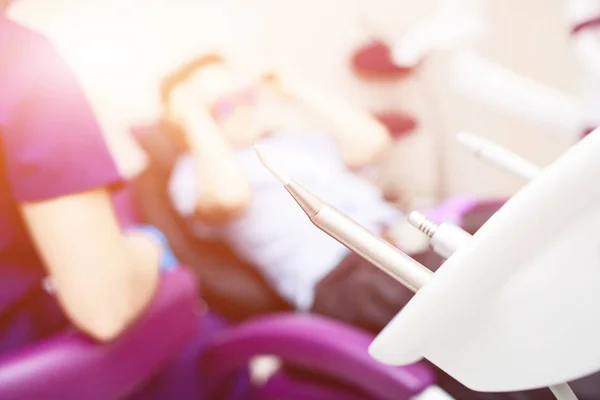 Escritório dentário desfocado. As ferramentas estão em primeiro plano. Um rapaz com óculos na cadeira dentária — Fotografia de Stock