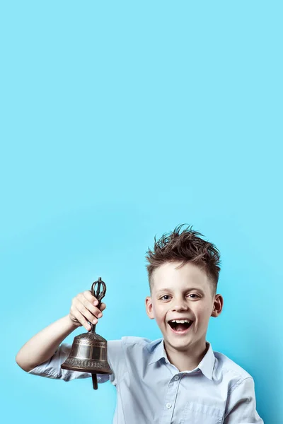 Un chico feliz con camisa ligera va a la escuela. Tiene una campana en la mano, que toca y sonríe . — Foto de Stock