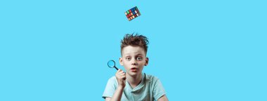hafif t-shirt bir çocuk elinde küçük bir büyüteç tutar ve bir Rubik küpü yukarıdan düşüyor.