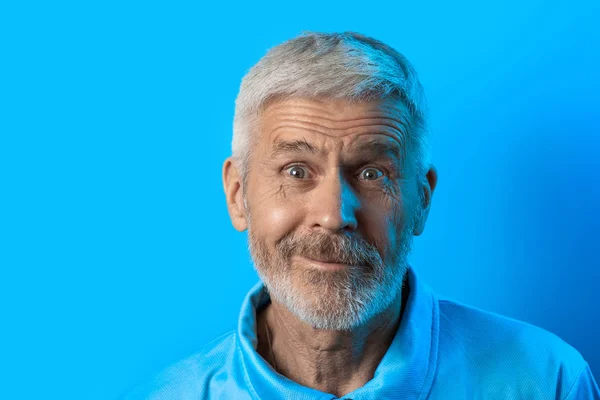 Retrato de hombre sorprendido y curioso de pelo gris con barba sobre fondo azul — Foto de Stock