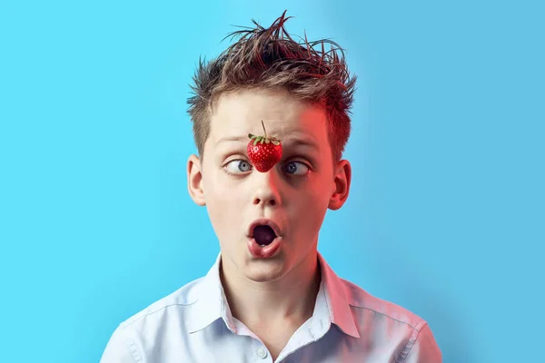 Overrasket dreng med en faldende jordbær klemt øjnene til næsen på en blå baggrund . - Stock-foto