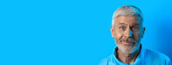 Retrato de hombre sorprendido y curioso de pelo gris con barba sobre fondo azul — Foto de Stock