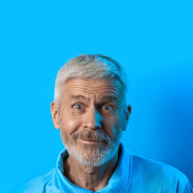 mavi bir arka plan üzerinde sakallı sürpriz ve meraklı gri saçlı adam portresi