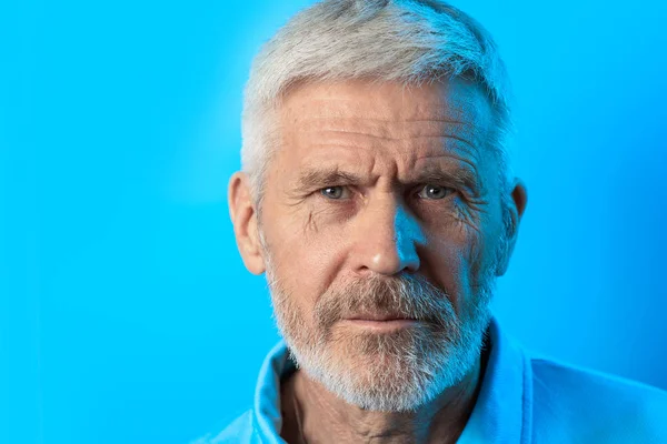 Portrait of a frowning gray-haired man with a beard on blue background — Stock Photo, Image