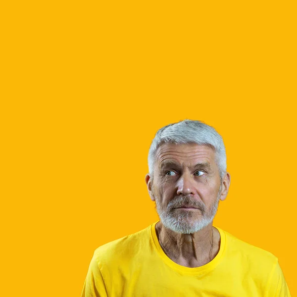 Portræt af overrasket og nysgerrig gråhåret mand med skæg på gul baggrund - Stock-foto