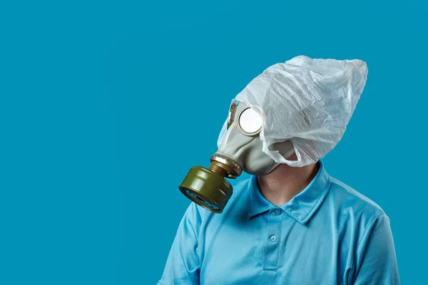 Un hombre con una máscara de gas y una bolsa de plástico en la cabeza simboliza la protección del medio ambiente contra la contaminación en el fondo azul — Foto de Stock