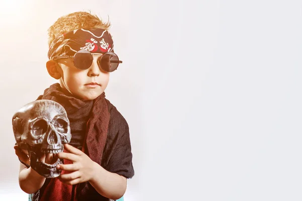 A boy rocker in black glasses, scarf, bandana and with a skull in his hands on a light background — Stock Photo, Image