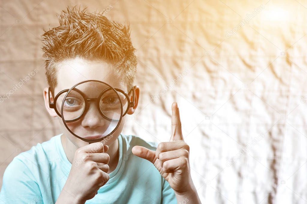 boy in a light t-shirt and glasses looking into a large magnifying glass