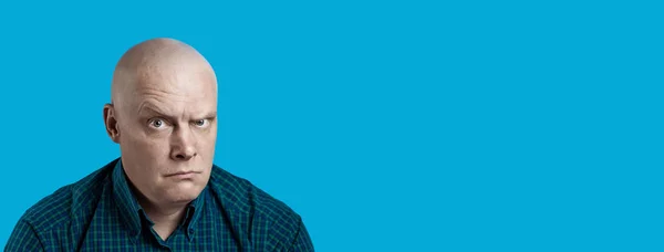 Porträtt av en skallig brutal man i en pläd skjorta på en blå bakgrund — Stockfoto