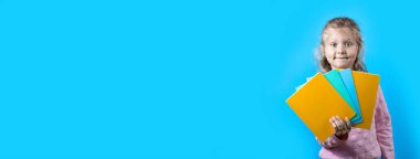 Yanaklarında gamzeler ve kıvırcık saçlı sevimli neşeli kız mavi arka plan üzerinde renkli okul defterleri tutan