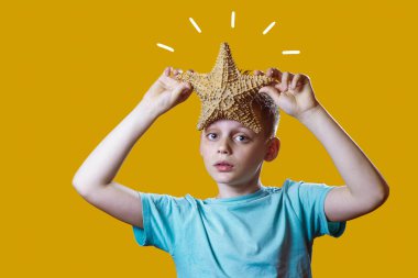 Sarı bir arka plan üzerinde bir denizyıldızı tutan hafif bir t-shirt bir çocuk