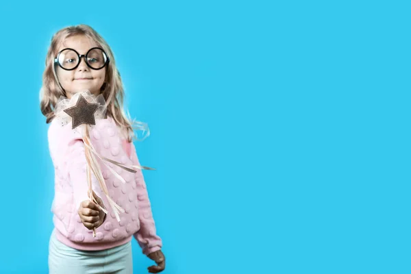 Flicka med glasögon och en trollstav säger en spell på blå bakgrund — Stockfoto