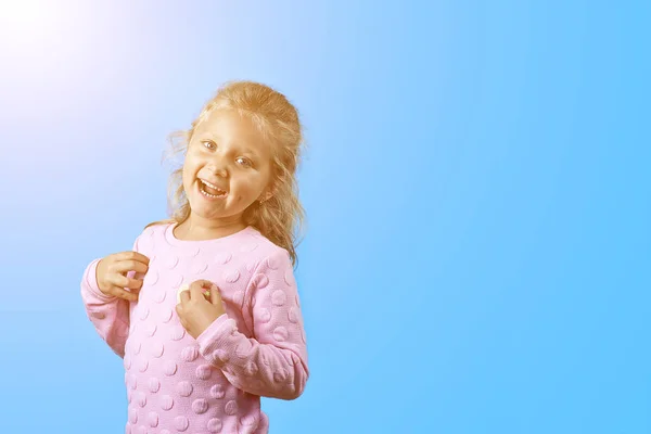 Cute wesoły dziewczyna z wgłębienia na policzkach i kręcone włosy uśmiecha się na niebieskim tle — Zdjęcie stockowe