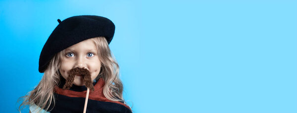 Funny girl in black beret, scarf and mustache on a stick on blue background
