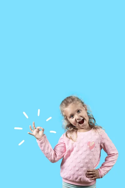 Cute wesoły dziewczyna z wgłębienia i kręcone włosy uśmiecha się i pokazuje OK znak na niebieskim tle — Zdjęcie stockowe