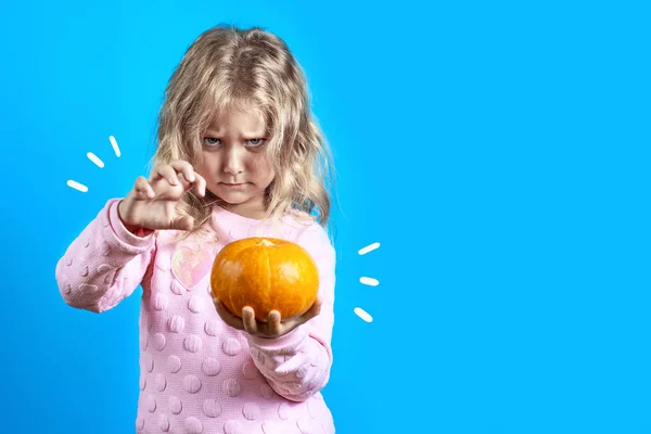 Söt häxa flicka med blonda hår frammanar över en pumpa på färgad bakgrund — Stockfoto