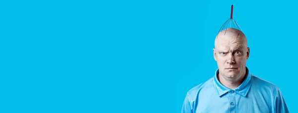 лысый жестокий человек чешет голову специальным устройством на синем фоне
