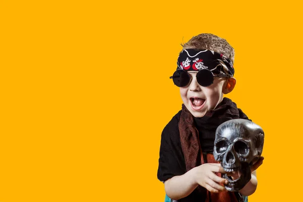 Un niño rockero en gafas negras, bufanda, bandana y con un cráneo en sus manos sobre un fondo brillante — Foto de Stock