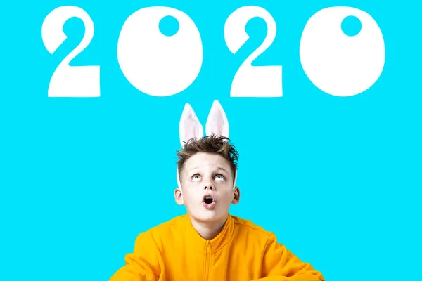 Overrasket dreng i en gul jakke og ører af en hare på blå baggrund. Store tal 2020 - Stock-foto