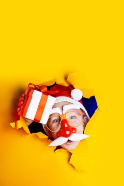 Kırmızı burunlu ve bıyıklı küçük neşeli Noel Baba hediye veriyor, sarı arka plandan kurtuluyor.