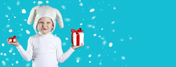 Valkoiseksi jänikseksi pukeutunut poika yrittää valita lahjan sinisellä taustalla — kuvapankkivalokuva