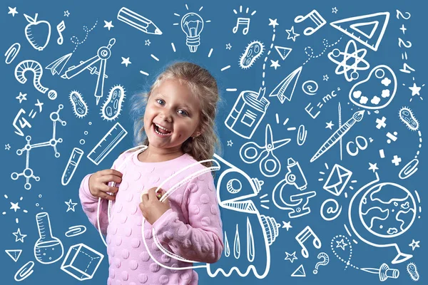 Cute cheerful girl with dimples on her cheeks and curly hair goes to school. Behind her satchel, where fly icons on the subject of study. — Stock Photo, Image